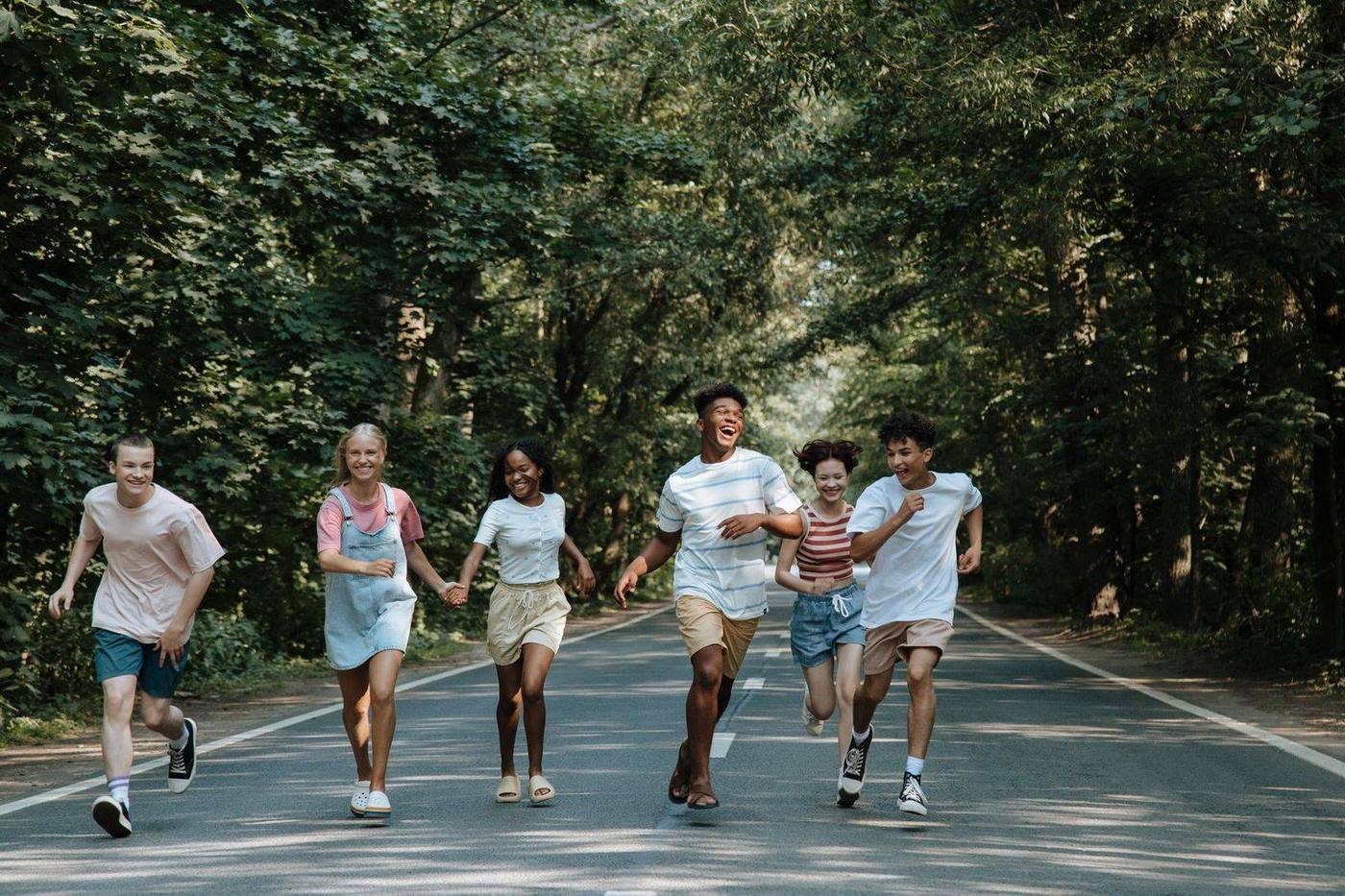 Grupo de adolescentes correndo e rindo em uma estrada arborizada