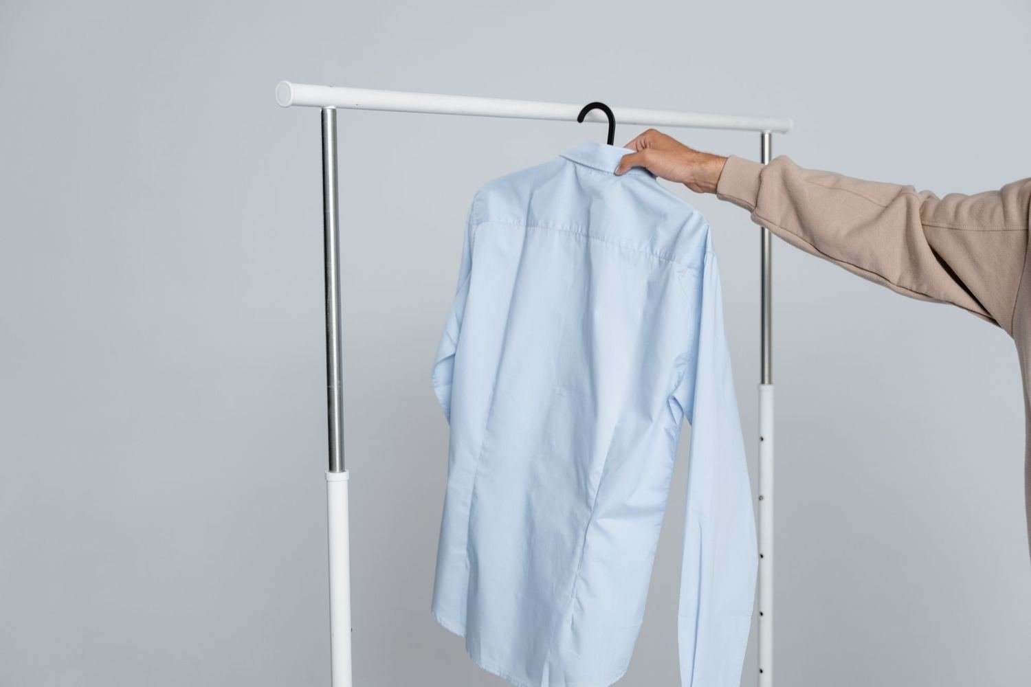 Mão pegando uma camisa social azul-clara pendurada no cabide