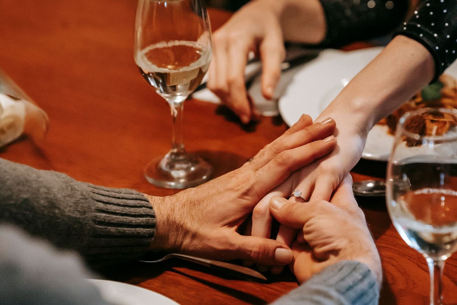 Mãos de um casal se tocando sobre a mesa de um jantar